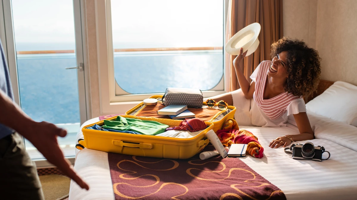 woman similing in cruise cabin with yellow suitcase